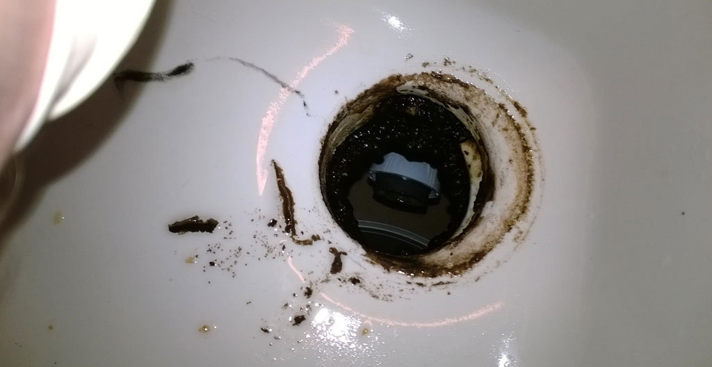 Mur de fondation de sous-sol résidentiel présentant infiltration d'eau active avec taches d'humidité brunâtres, moisissure noire et fissure laissant suinter de l'eau sur sol humide